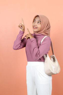 Güzel, genç Asyalı bir kadın gülümseyerek, dişlerini gösteriyor ve bir çanta taşıyor. 