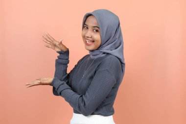 Güzel, genç Asyalı bir kadın, elleri yanında gülümseyen bir yüzle dişlerini gösteren bir şey sunuyor.