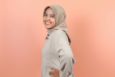 Güzel, genç bir Asyalı kadın ellerini beline koyuyor iki eliyle yandan gülümseyerek dişlerini gösteriyor.