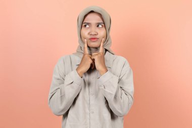 Güzel, genç Asyalı bir kadın yanağına dokunuyor. Kafası karışmış iki parmağı da yukarı bakıyor.