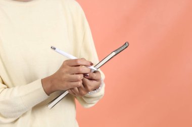 Kremalı süveter giyen neşeli Asyalı Müslüman kadın not defterini açıyor ve şeftali arka planda izole edilmiş bir şeyin üzerine gülümsüyor. 