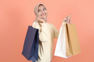 Krem rengi kazaklı neşeli Asyalı Müslüman kadın şeftali arka planda izole edilmiş alışveriş çantaları tutuyor. Dünya Tüketici Hakları Günü kavramı. 