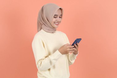 Gülümseyen, süveter ve tesettürlü, cep telefonu kullanan, cep telefonu kullanan, SMS yazan, mesaj yazan güzel Asyalı Müslüman kadın. İnsanlar dini yaşam tarzı kavramları