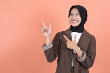 Kahverengi takım elbiseli, tesettürlü ve tesettürlü güzel Asyalı kadın uzayı kopyalamak için parmağını kenara kaldırıyor. İnsanlar dini yaşam tarzı konsepti