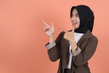 Kahverengi takım elbiseli, tesettürlü ve tesettürlü güzel Asyalı kadın uzayı kopyalamak için parmağını kenara kaldırıyor. İnsanlar dini yaşam tarzı konsepti