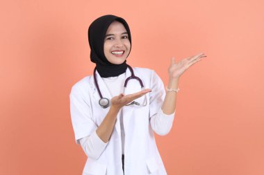 Beyaz önlüklü, belinde steteskop olan güzel Asyalı Müslüman kadın doktor. Fotokopi alanı dışında bir şey. Kadın hastane çalışanı kameraya bakıp gülümsüyor.