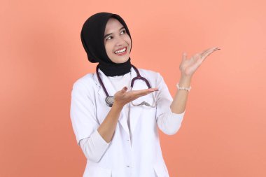 Beyaz önlüklü, belinde steteskop olan güzel Asyalı Müslüman kadın doktor. Fotokopi alanı dışında bir şey. Kadın hastane çalışanı kameraya bakıp gülümsüyor.