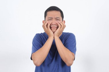 Korkmuş Asyalı adam korkudan titriyor ve parmaklarını yanağına çiviliyor. Kamera karşısında korkmuş ve güvensiz görünüyor. Panik içinde korkmuş bir adam endişeli, korkunç bir kazaya tanık olmuş, korku filmi seyrediyor.