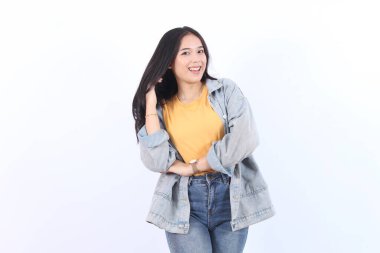 Neşeli Asyalı kadın, özgüvenli bir şekilde gülümseyen, elleri saçında, mavi ceketli ve sarı tişörtlü, izole edilmiş beyaz arka planda kameraya bakan.