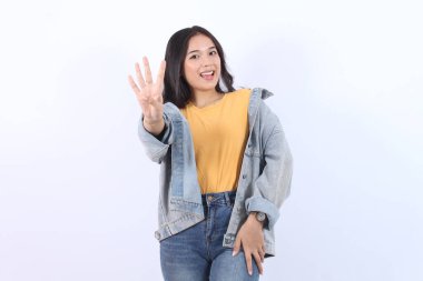 Asyalı güzel bir kadın mavi ceketli, sarı tişörtlü, 4 numarayı gösteren ve beyaz arka planda dört numarayı işaret eden. 