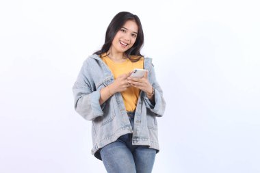 Akıllı telefon kullanan güzel bir Asyalı kadın izole edilmiş beyaz arka planda duruyor. Heyecanlı genç Asyalı alışverişi cep telefonuyla yapıyor. Akıllı telefondan oyun oynanıyor