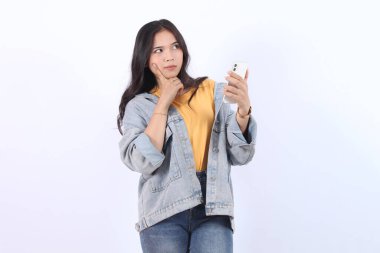 Güzel Asyalı kadın akıllı telefon görüntüsü vermeyi düşünüyor. İzole edilmiş beyaz arka planda duran kadın duruşu. Çekici 25 yaşlarında bir genç kız.