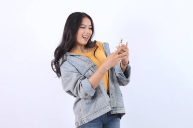 Güzel Asyalı kadın akıllı telefon görüntüsü vermeyi düşünüyor. İzole edilmiş beyaz arka planda duran kadın duruşu. Çekici 25 yaşlarında bir genç kız.