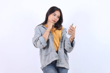 Güzel Asyalı kadın akıllı telefon görüntüsü vermeyi düşünüyor. İzole edilmiş beyaz arka planda duran kadın duruşu. Çekici 25 yaşlarında bir genç kız.