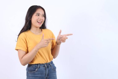Güzel, genç Asyalı bir kadın gülümseyen yüzüyle ve mutlu yüzüyle boşluğu işaret ediyor. Güzel kız tatmin olmuş bir ürün gibi davranıyor, beyaz arka planda izole edilmiş reklamcılık için kullanıyor.