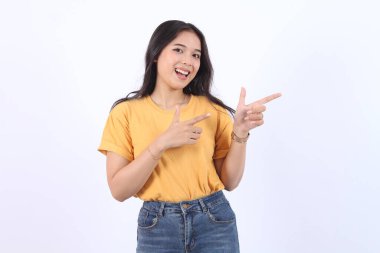 Güzel, genç Asyalı bir kadın gülümseyen yüzüyle ve mutlu yüzüyle boşluğu işaret ediyor. Güzel kız tatmin olmuş bir ürün gibi davranıyor, beyaz arka planda izole edilmiş reklamcılık için kullanıyor.