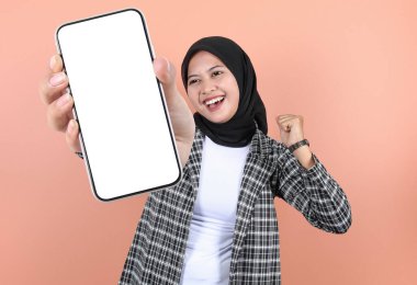 Gülümseyen genç Asyalı güzel bir kadın reklam için cep telefonu ekranını gösteriyor ve şeftali arka planda izole edilmiş başarıyı kutluyor. Halk Yaşam Tarzı Konsepti
