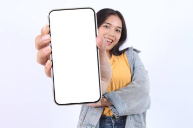 Gülümseyen genç Asyalı kadın, günlük sarı tişörtler giyip reklam için cep telefonunu ve beyaz arka planda izole edilmiş kendine güvenen pozu gösteriyor. Halk Yaşam Tarzı Konsepti