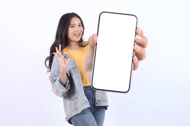 Gülümseyen genç Asyalı kadın, günlük sarı tişörtler giyip reklam için cep telefonunu göstererek beyaz arka planda izole edilmiş bir şekilde işaret veriyor. Halk Yaşam Tarzı Konsepti
