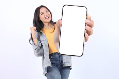 Gülümseyen, sarı tişört giyen, reklam için cep telefonunu gösteren ve beyaz arka planda izole edilmiş başarıyı kutlayan güzel bir Asyalı kadın. Halk Yaşam Tarzı Konsepti