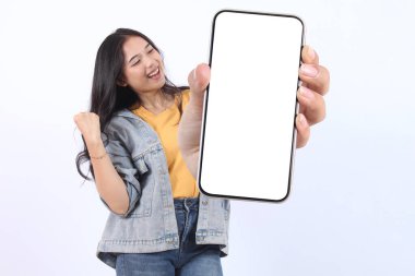 Gülümseyen, sarı tişört giyen, reklam için cep telefonunu gösteren ve beyaz arka planda izole edilmiş başarıyı kutlayan güzel bir Asyalı kadın. Halk Yaşam Tarzı Konsepti