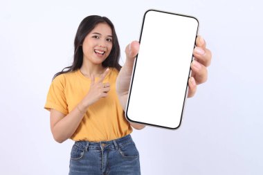 Gülümseyen, sarı tişört giyen, reklam için cep telefonu ekranı gösteren ve beyaz arka planda izole edilmiş bir telefonu işaret eden güzel bir Asyalı kadın. Halk Yaşam Tarzı Konsepti