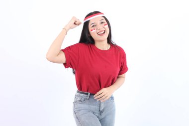 Mutlu ve başarılı bir ifadeyle heyecanlı genç Asyalı kadın kırmızı başlık takıyor ve beyaz arka plan ile izole edilmiş bayraklar takıyor, bir elini Endonezya 'nın bağımsızlık günü konseptini sıkıca kavrıyor..