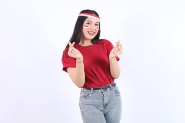 Heyecanlı genç Asyalı kadın, Endonezya 'nın bağımsızlık günü konseptini kutlamak için kırmızı başlık ve bayrak takmış parmaklarıyla kalp işareti gösteriyor..