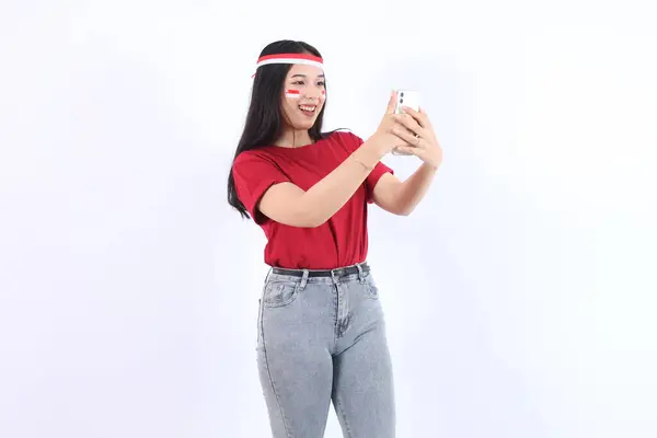 stock image Excited young Asian woman holding mobile phone with selfie isolated over white background. Celebrate Indonesian independence day on 17 August