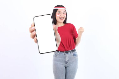Kırmızı beyaz bayraklı genç Asyalı kadın reklam ve Endonezya 'nın bağımsızlığını kutlamak için 17. Gün Agustus' u tanıtmak üzere ekranda cep telefonu gösteriyor. Merdeka kavramı