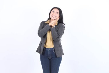 Beyaz arka planda tek başına duran, sıradan takım elbiseli, mutlu, güzel Asyalı iş kadını. Ellerinizi yanaklarınızın altında tutun ve boş alanlara bakın..