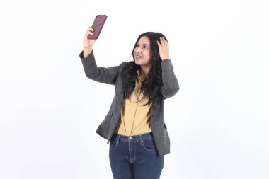Mutlu iş Asyalı kadın elinde telefonla selfie çekiyor ve saçlarına dokunuyor, gri ceket giyiyor.