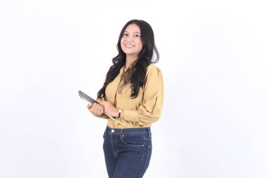 Sarı gömlekli ve kot pantolonlu kadın elinde bir tablet tutuyor. Gülümsüyor ve mutlu. İş kadını Asyalı kadın 