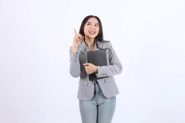 Gri ceketli kadın elinde siyah bir defter tutuyor ve gökyüzünü işaret ediyor. Gülümsüyor ve bir şey için heyecanlı ya da heyecanlı. İş kadını Asyalı kadın