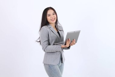 Güzel bir kadın sunum için beyaz bir arkaplan önünde dizüstü bilgisayar tutuyor. Gri bir ceket ve kot pantolon giyiyor. İş kadını Asyalı kadın