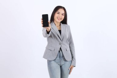 Kadın elinde bir cep telefonu tutuyor ve gülümsüyor. Gri bir ceket ve kot pantolon giyiyor. Beyaz arka planda izole edilmiş Asyalı iş kadını.