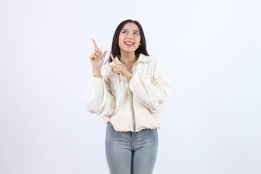 Krem rengi ceket ve kot pantolon giyen güzel bir kadın. Gülümsüyor ve boş alanı işaret ediyor. beyaz üzerine izole