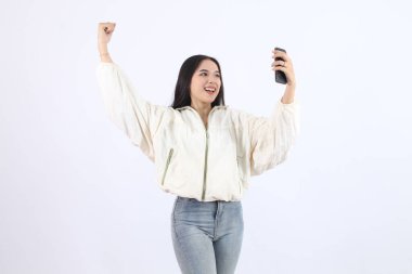 Kadın, Smartphone ile Selfie çekerken Başarı Kutlaması Yapıyor ve Beyaz Arkaplanda Tutkulu Bir El Kaldırıyor