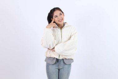 Kadın, fikri düşünür, parmağıyla başını gösterir, mutlu bir şekilde gülümser ve ilhamla yukarıya bakar.