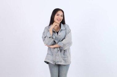 Kadın gülümseyip poz veriyor. Beyaz arka planda kot ve kot pantolon giyiyor.