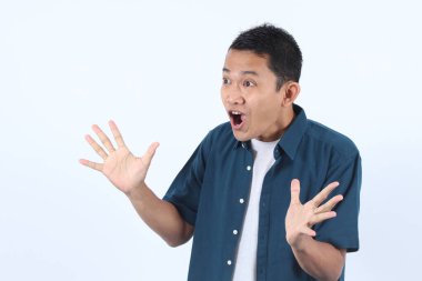 Mavi tişörtlü yetişkin Asyalı adam ellerini uzatarak şaşırmış bir yüz ifadesi takındı. Heyecan ya da şok kavramı, beklenmedik bir haber aldı ya da şaşırtıcı bir olay yaşadı.