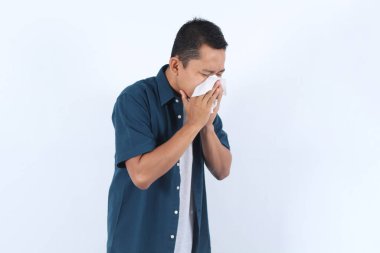 Adult Handsome Asian Man wearing blue shirt Blows Nose with Tissue, Suffering from Cold or Allergies Quickly and Easily with Common Symptoms clipart