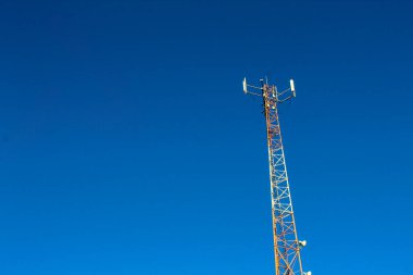 Arka planda mavi gökyüzü olan uzun bir kule. Kule turuncu renkli ve tepesinde bir hava durumu istasyonu var.