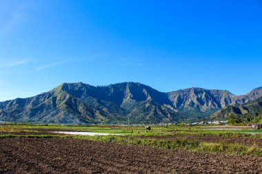 Açık mavi gökyüzü olan güzel bir dağ sırası. Dağlar ağaçlarla çevrili ve gökyüzü berrak ve parlak.