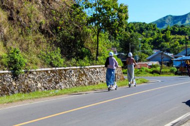 İki kadın yolda scooter kullanıyor. Sahne neşeli ve neşeli.