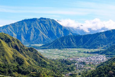 Sembalun Tepesi, Lombok Endonezya sıradağları ve aşağıdaki vadide bir kasaba. Gökyüzü açık ve dağlar yemyeşil ağaçlarla kaplı.