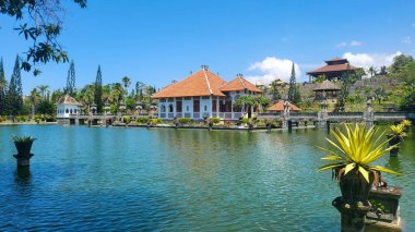 Arka planda beyaz bir ev olan güzel bir göl. Ev bir bahçe ile çevrilidir ve gölün etrafında birkaç saksı bitkisi vardır. Sahne huzurlu ve huzurlu Taman ujung, Karangasem Bali, Endonezya 27 Ağustos 2023