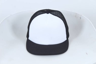 Siyah-beyaz kamyoncu şapkası, örgü sırtlı, beyaz sandalyeye yerleştirilmiş. Marka modelleri, giyim tasarımları ya da promosyon görselleri için ideal. Ticari kullanım ve ürün sergilenmesi için yüksek çözünürlüklü resim.