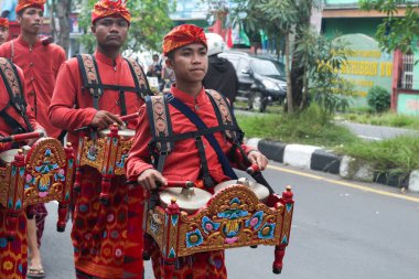 Praya, Lombok, Batı Nusa Tenggara, Endonezya, 19 Nisan 2025. Cidden Asyalı bir adam, geleneksel Lombok kostümleri giyerek Nyongkolan etkinliği sırasında ana caddede yeşil Beleq davulunu çalıyor..
