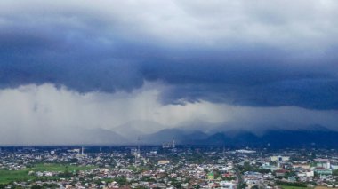 Mataram, Lombok, Endonezya üzerinde kasvetli, yağmurlu bir gökyüzü. Karanlık tepeler ve çatılar sisli şehir manzarasına karışıyor..